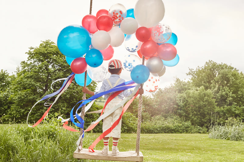 Child on a wooden swing with colorful balloons in a sunny park.