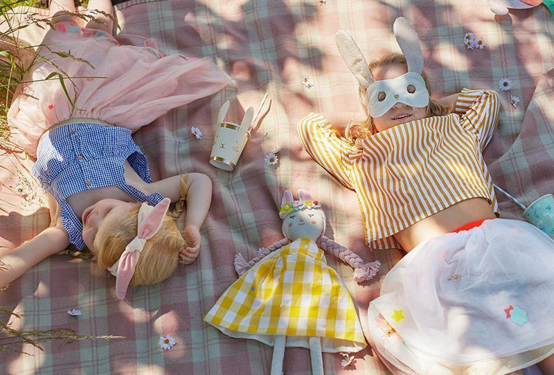 Two children in bunny masks lie on a plaid blanket among Easter decorations.