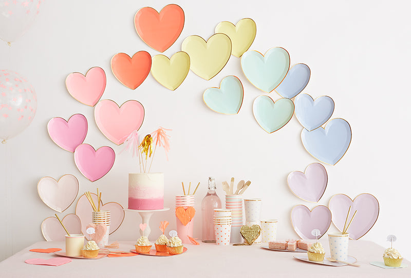 Pastel heart garland arches over a dessert table with a pink cake and cupcakes in soft pink and peach tones.