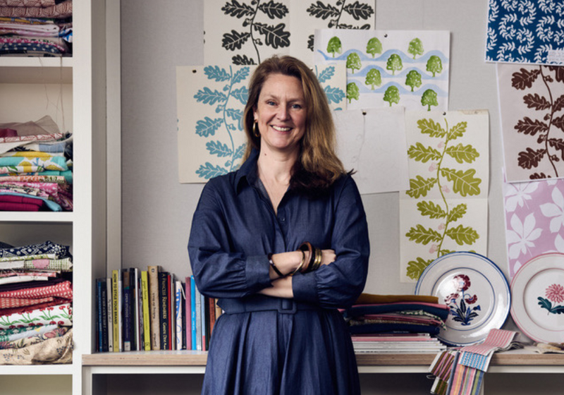 Portrait of textile designer Molly Mahon in her studio, standing with arms crossed among fabric swatches and wall prints.