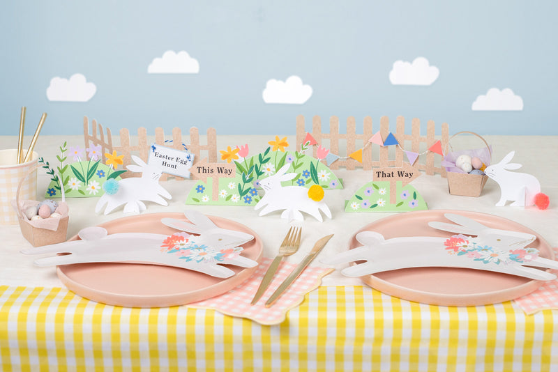 A yellow and white striped table is decorated with pink and leaping bunny plates. Cardboard floral and bunny decorations are placed in the center.