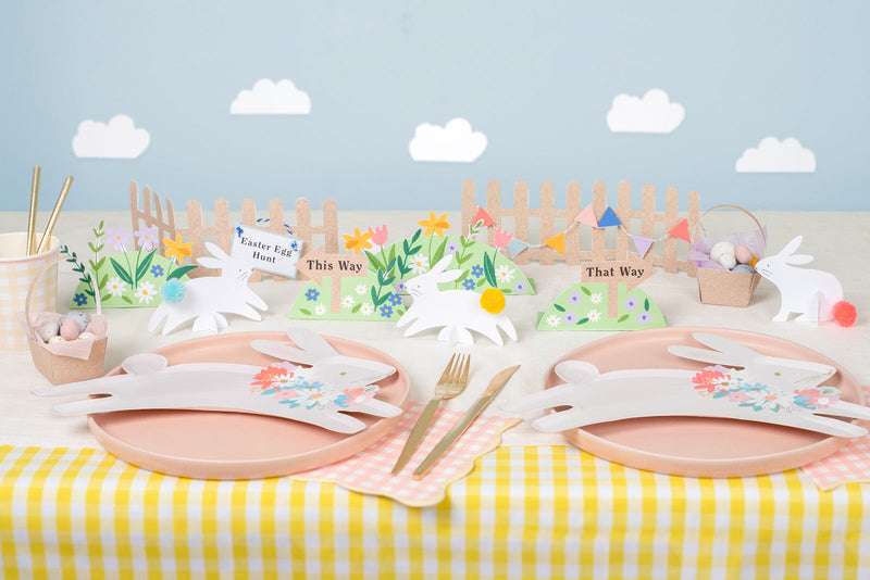 A yellow and white striped table is decorated with pink and leaping bunny plates. Cardboard floral and bunny decorations are placed in the center.