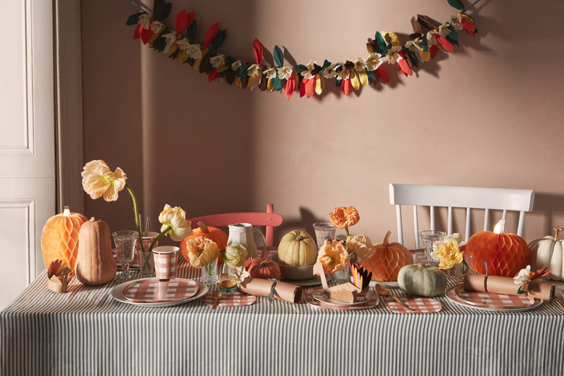 A table laid with Thanksgiving-inspired tableware, including orange gingham plates and napkins, honeycomb pumpkins and paper turkey crackers.