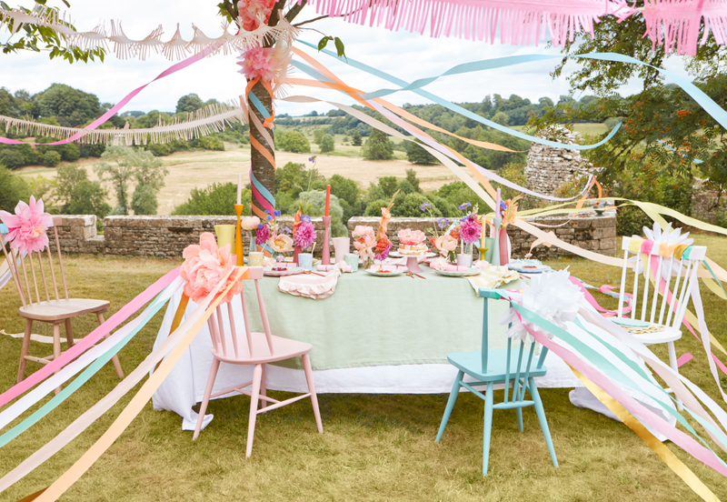 Pastel outdoor dining setup for a summer dinner party with ribbons and floral centerpieces.