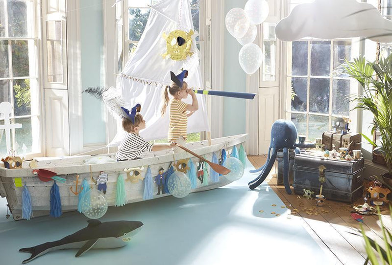Kids in a bright room navigate a decorated white boat with sails and sea themed party decor and balloons