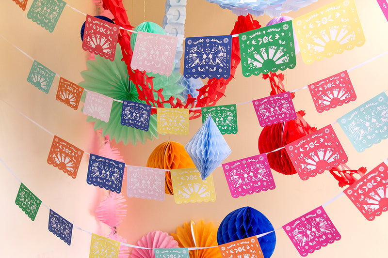 Papel picado garlands swing from the ceiling with rainbow honeycomb streamers in the background.