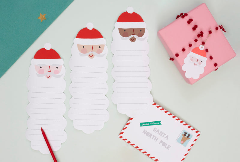 3 lined pages in the shape of Santas are placed on a light green background, with a pink package and Santa gift tag besides them.