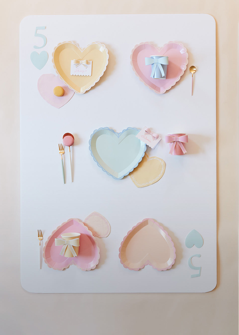 A card of the 5 of hearts is created out of pastel heart plates in colors of yellow, green, pink, and blue.