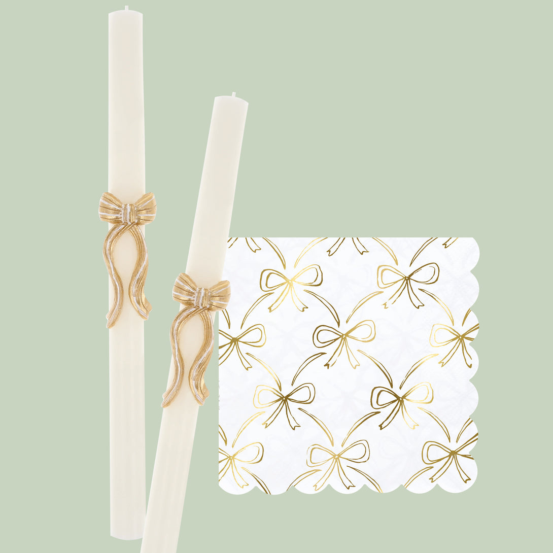 Our golden Christmas host gift set includes two table candles, with gold stripy bow details, and a pack of paper napkins with gold bow designs. Image1